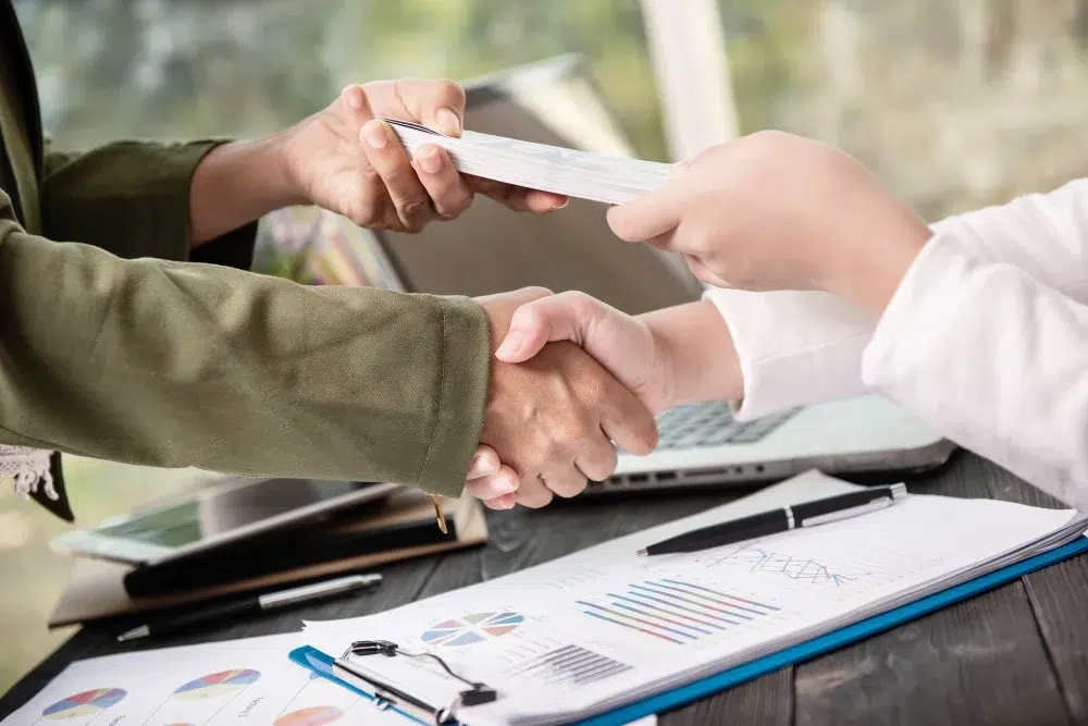 Two people shaking hands over a desk covered with papers, symbolizing agreement or collaboration.