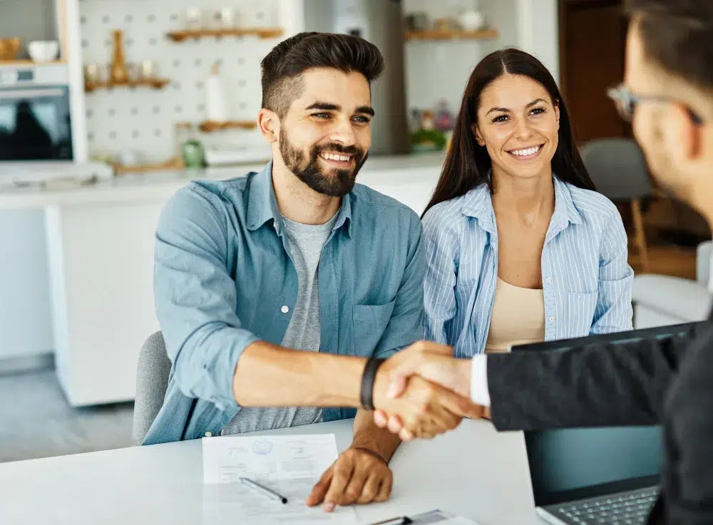A man and woman shaking hands across a desk, symbolizing agreement or partnership in a professional setting.