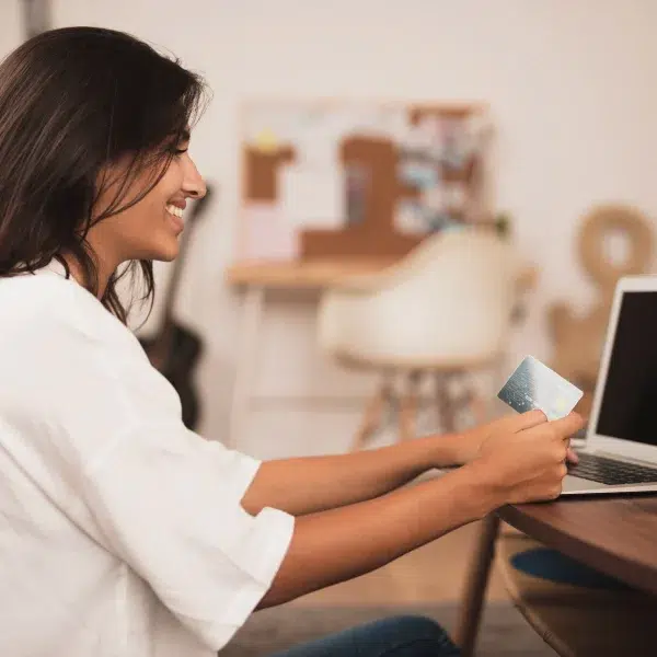 A woman sits at a table with a laptop and credit card, comparing online loans to traditional banks.