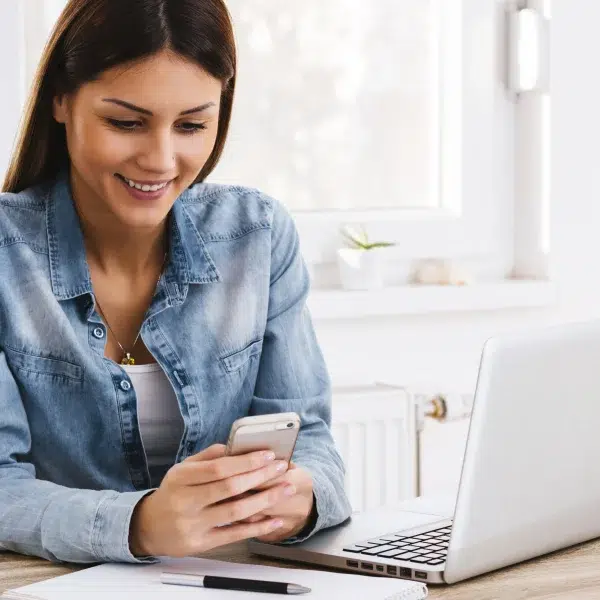 A woman at a table using a laptop and cell phone, comparing online loans and traditional banks.