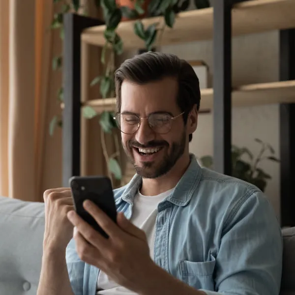 A smiling man with glasses and a beard using a phone.
