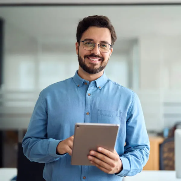 Jeune homme souriant dans un bureau, tenant une tablette électronique