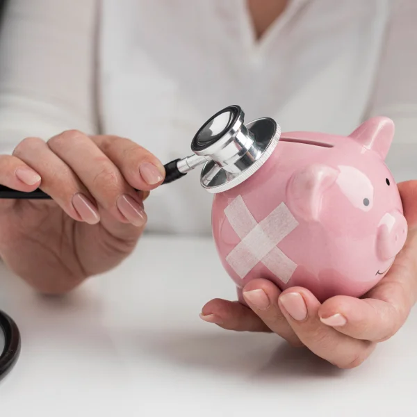 Une femme tenant un stéthoscope au-dessus d'une tirelire, symbolisant la santé financière et le prêt d'urgence sans refus.