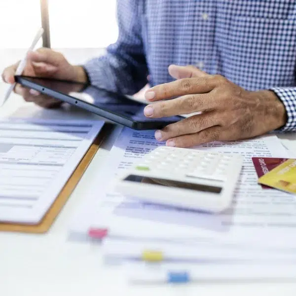 A man analyzing his credit score using a tablet and calculator at a desk.