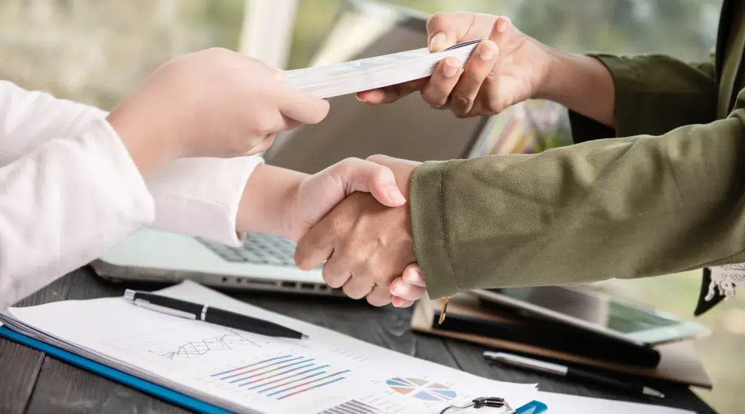 Deux personnes se serrent la main au-dessus d'un bureau avec des documents, symbolisant un accord ou une collaboration.