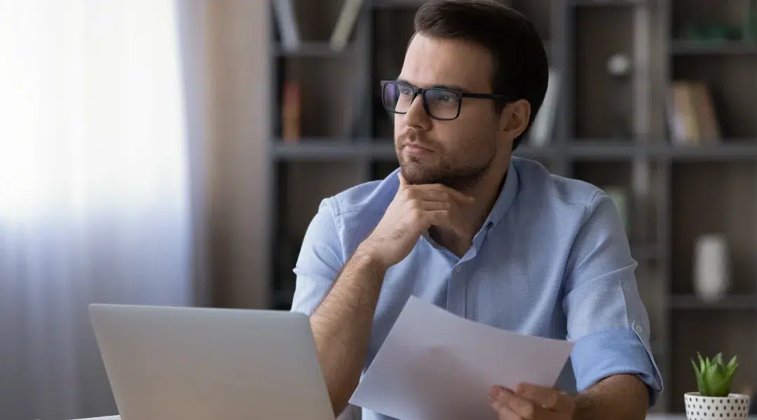 A man in glasses sits at a desk with a laptop, contemplating options for an instant loan.